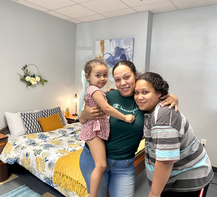 A woman and her daughters smiling in front of a renovated bedroom