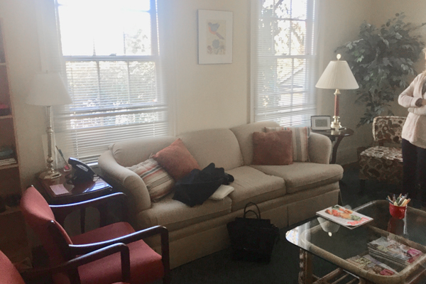 A light colored couch with two bright windows behind it