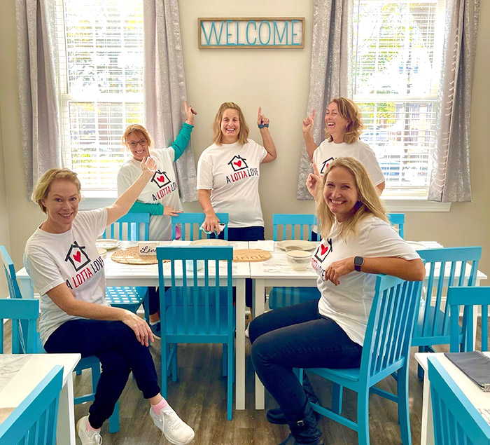 Volunteers smiling and pointing to a welcome sign