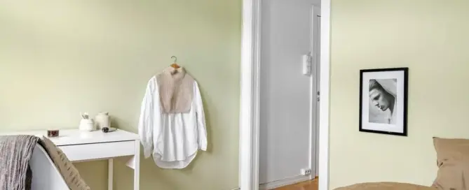 Soft green trauma informed paint colors in a minimalist bedroom with cozy bedding and modern decor